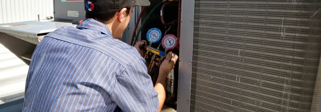 HVAC technician servicing a condenser unit in Littleton